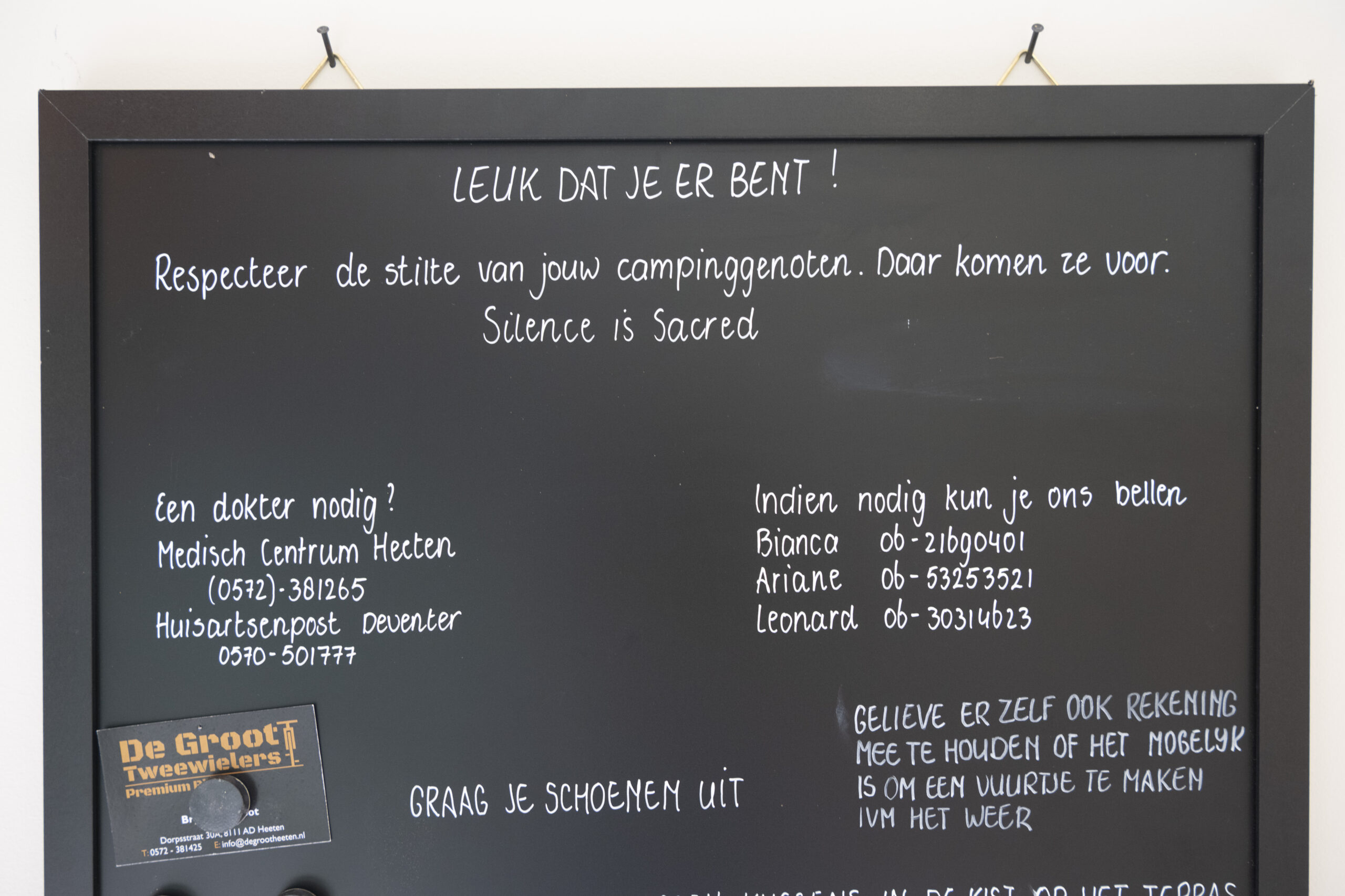 Chalkboard sign with English and Dutch text about respecting campers' quiet and listing contact numbers.
